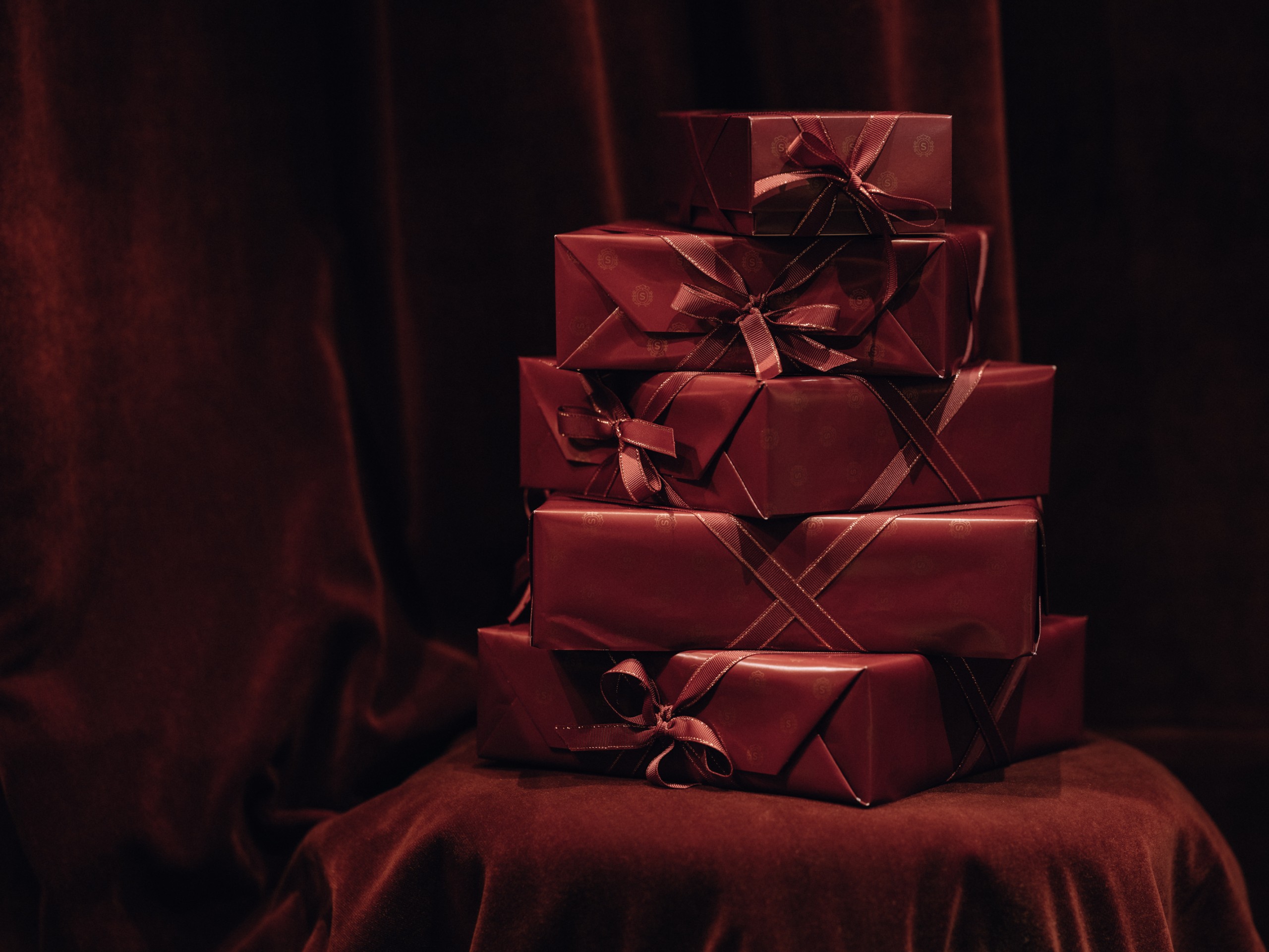 A stack of five elegant gifts wrapped in dark red paper with contrasting ribbons and bows.