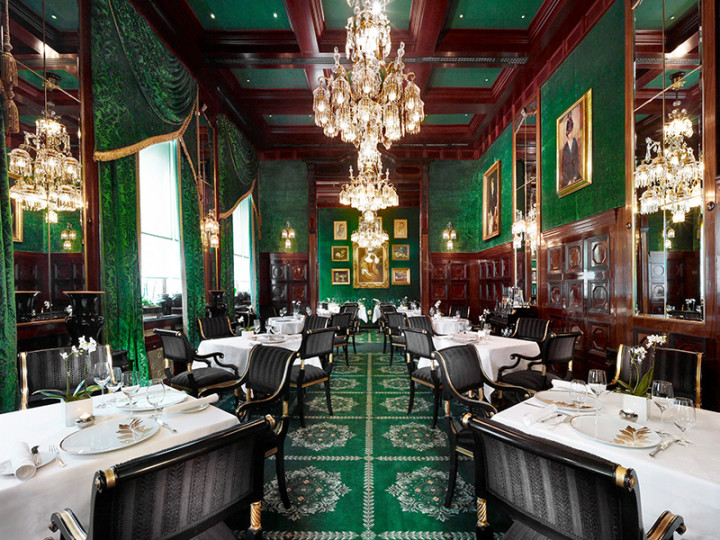 Ein eleganter Speisesaal mit üppigem Interieur, smaragdgrünem Dekor, Kristalllüstern und klassisch gedeckten Tischen