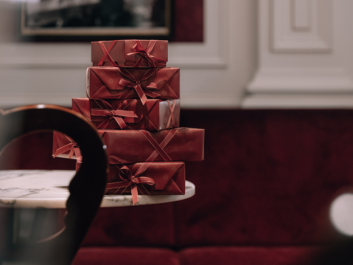Stack of elegantly wrapped, red original Sacher-Torte boxes on a marble table in front of a velvet-red bench